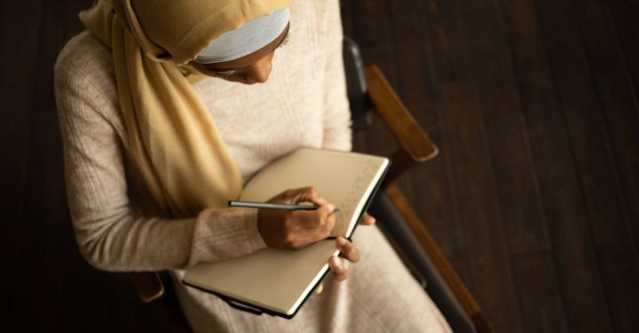 Workplace Culture - Crop black Muslim woman writing in planner