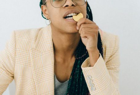 Financial Management - Woman in a Beige Coat Biting a Gold Chocolate Coin while Sitting by the Table