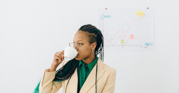 Investment Strategies - Woman in Beige Coat Drinking from a White Cup in Front of Her Work Desk