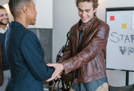 Investor - Man in Brown Leather Jacket Shaking Hands with Woman in Black Blazer