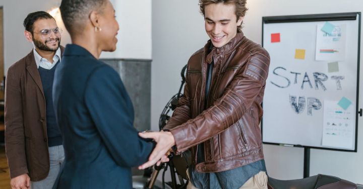 Investor - Man in Brown Leather Jacket Shaking Hands with Woman in Black Blazer