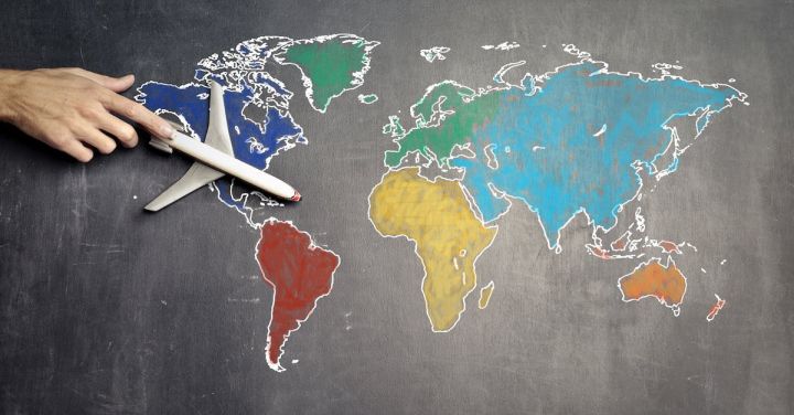 Business Strategies - Top view of crop anonymous person holding toy airplane on colorful world map drawn on chalkboard