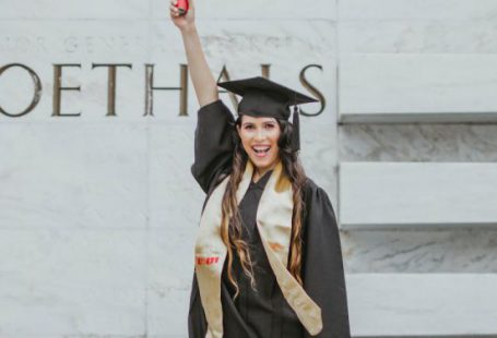 Success - Photo of Smiling Woman in Black Academic Dress Standing In Front of Marble Wall Holding Up Diploma
