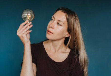 Idea - Enthusiastic female in casual clothes standing against blue background and looking at glowing light bulb
