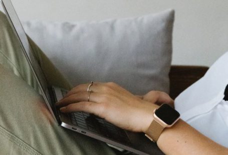 Business Connections - Side view of crop unrecognizable female freelancer in casual clothes and smartwatch lying on comfortable sofa and working remotely on laptop