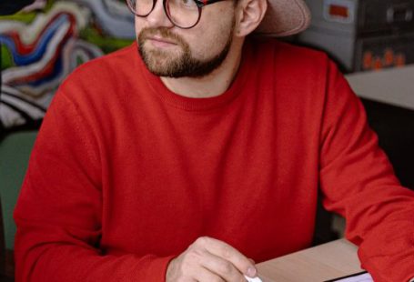 Idea - Vertical Shot of a Man in a Hat and Red Sweatshirt Discussing an Interior Design Project on Workshop