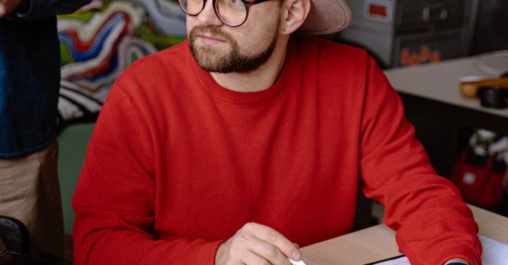 Idea - Vertical Shot of a Man in a Hat and Red Sweatshirt Discussing an Interior Design Project on Workshop