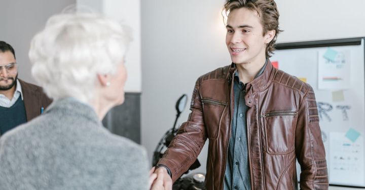 Investor - Man in Brown Leather Jacket Shaking Hands with Woman in Gray Blazer