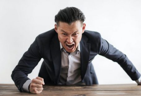 Boss - Expressive angry businessman in formal suit looking at camera and screaming with madness while hitting desk with fist
