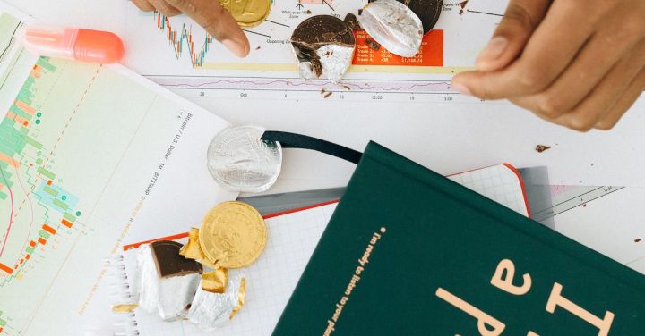 Management - Person Holding a Gold Chocolate Coin on the Table with a Green Book